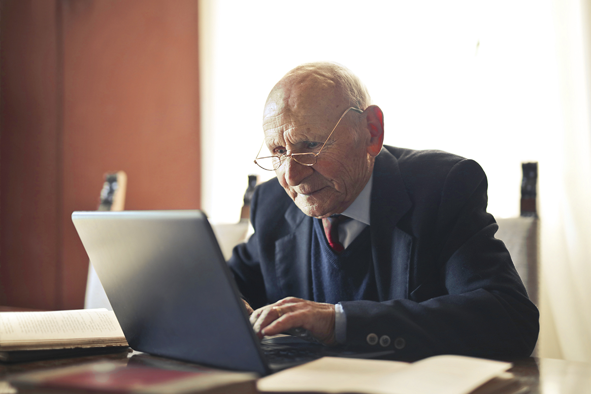 äldre man sitter framför sin laptop vid skrivbordet